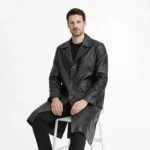 Man seated wearing black leather trench coat showing elegant drape, accessible pockets, refined styling, sophisticated outerwear