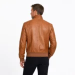 Side profile of tan brown leather bomber jacket showing raglan sleeves, ribbed waistband and cuffs, buckle collar, and classic bomber cut
