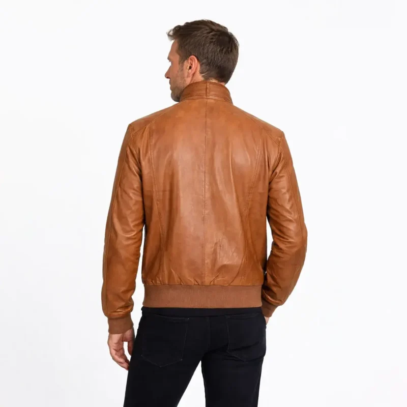 Side profile of tan brown leather bomber jacket showing raglan sleeves, ribbed waistband and cuffs, buckle collar, and classic bomber cut