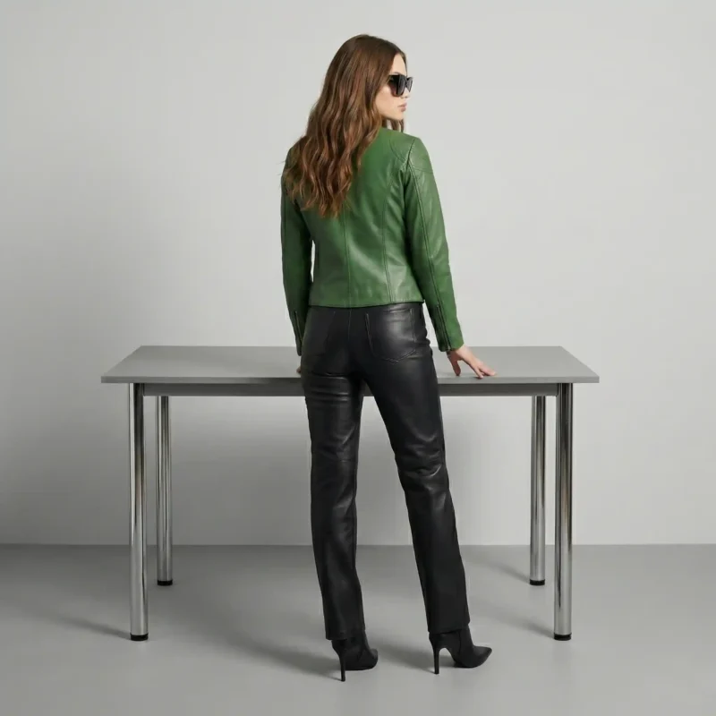 Woman wearing emerald green leather jacket with black leather straight-leg pants, ankle boots, and sunglasses for chic color-blocked look