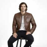 Man seated wearing brown leather cafe racer jacket showing comfortable raglan sleeve movement, natural leather draping, chest pocket accessibility, and unrestricted fit while sitting