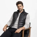 Man seated wearing black leather puffer vest - Ironcrest Obsidian Leather Field Vest - showing comfortable fit, quilted insulation, versatile layering piece over sweater