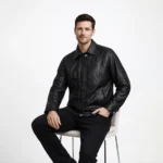 Man seated wearing black leather bomber jacket showing comfortable relaxed fit, accessible diagonal pockets, natural leather draping, ribbed hem flexibility, and easy movement while sitting