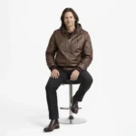 Man wearing brown leather hooded bomber jacket while seated, showing comfortable fit and functional hood design