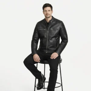 Man seated wearing black leather moto jacket with quilted sleeves showing comfortable fit, dramatic ribbed texture detail, natural leather movement, and striking visual presence while sitting