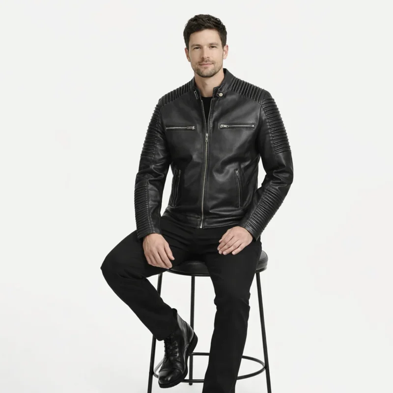 Man seated wearing black leather moto jacket with quilted sleeves showing comfortable fit, dramatic ribbed texture detail, natural leather movement, and striking visual presence while sitting