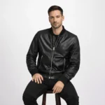 Man wearing black leather bomber jacket while seated, demonstrating comfortable fit, ribbed trim detail, and supple leather construction