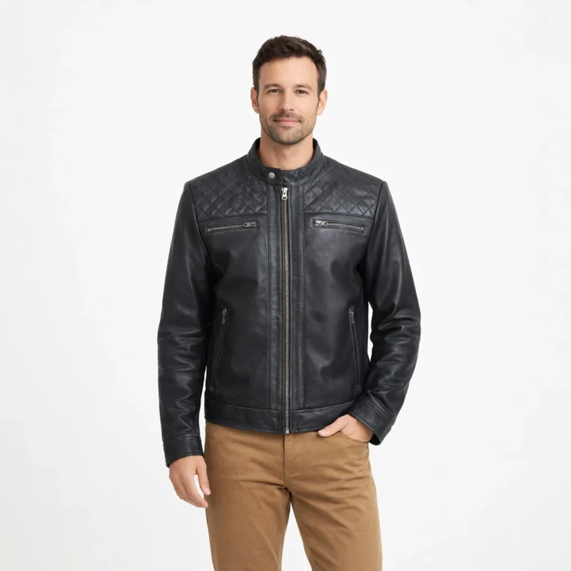Man wearing black leather racer jacket with diamond quilted collar and shoulders, center zip closure, chest zip pockets, and tan chinos on light gray background