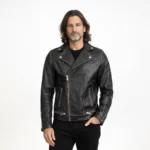 Man wearing distressed black leather motorcycle jacket with asymmetric brass zipper closure, wide lapel collar, multiple zip pockets, and vintage hardware on light background