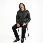 Man seated wearing distressed black leather biker jacket with all black outfit, demonstrating comfort, flexibility, and maintained structure while sitting