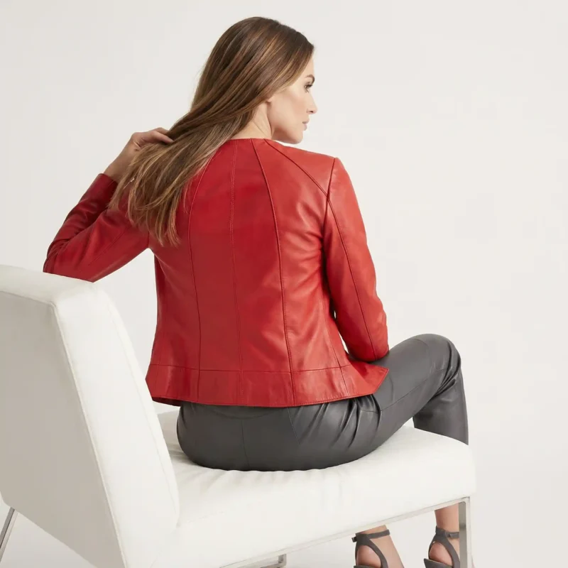 Woman wearing red leather bomber jacket seated on modern white chair, styled with gray leather pants and heels for sophisticated look