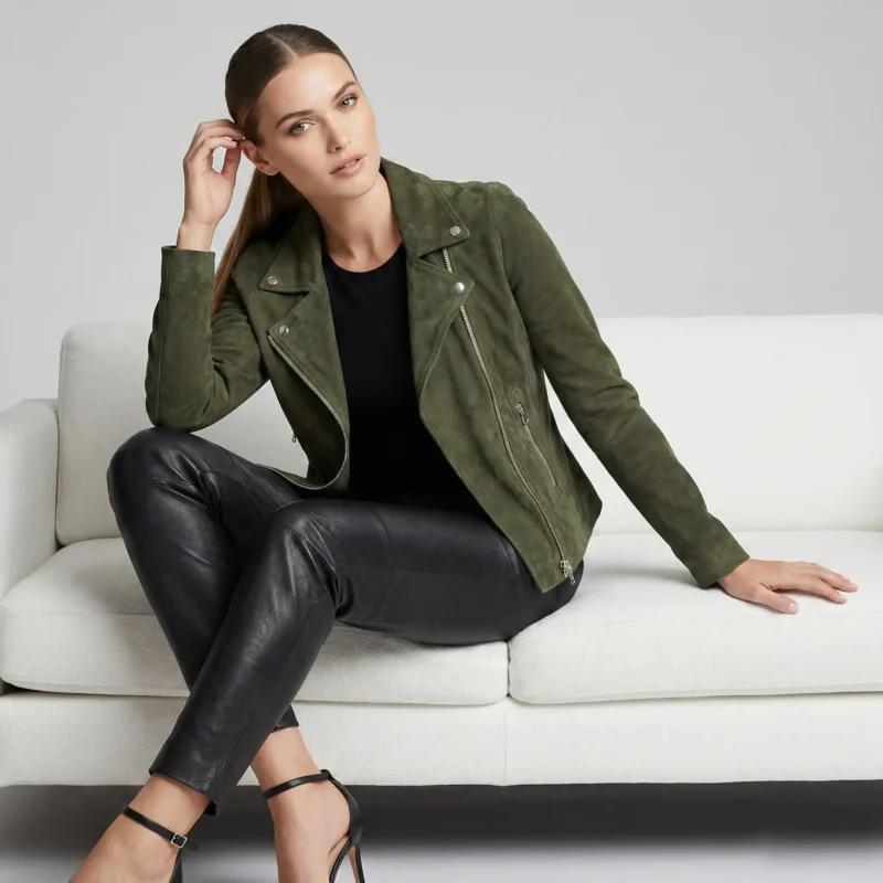 Premium Suede Moto Leather Jacket Front View - Women's Asymmetric Biker Jacket Woman wearing olive green suede motorcycle jacket - Premium Suede Moto Leather Jacket - with asymmetric zipper closure, notch lapels, silver hardware, black leather pants, and black top on white couch