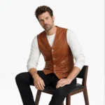 Man seated wearing tan brown leather vest showing comfortable tailored fit, accessible pockets, versatile layering piece