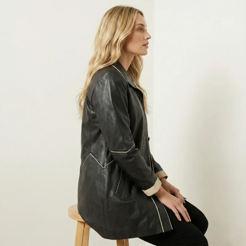 Side view of women’s black leather coat showing beige trim, tailored waist, and mid-length cut